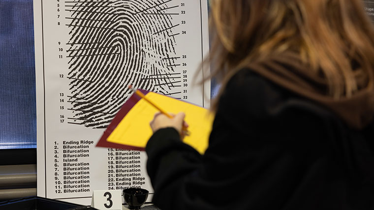 A student takes notes as she surveys a large printout of a fingerprint.